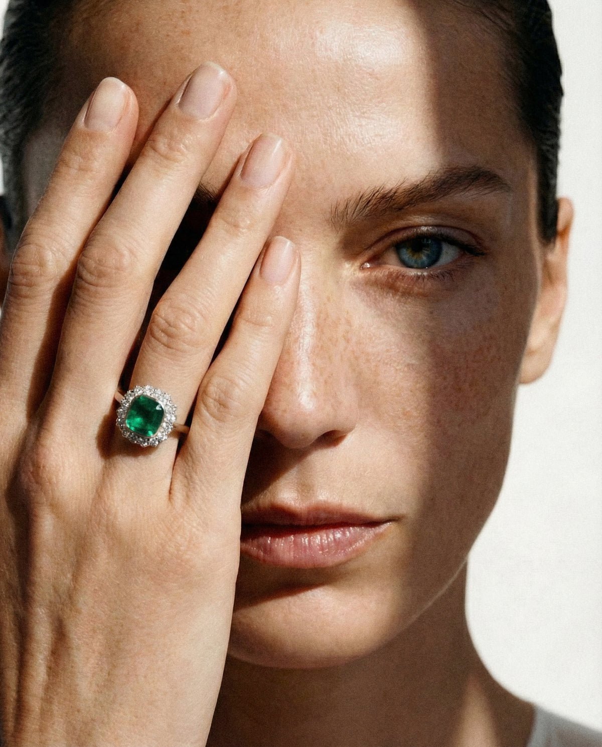 An emerald ring worn on a hand held across the face